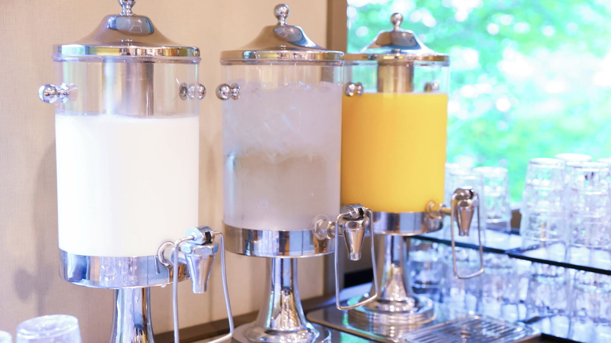 Three beverage dispensers with spouts, connected to a bar area with glasses.