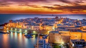 A coastal town at sunset with historic buildings, a fortified wall, and a marina with boats. - La Casa del Turista (Gallipoli)