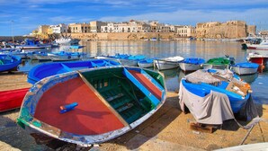 A harbor with numerous boats docked, a historic building in the background, and a clear sky. - La Casa del Turista (Gallipoli)