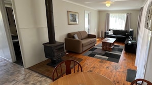 A cozy living room with a wood-burning stove, a sofa, a dining table with chairs, and a view of the outdoors through a window. - Bestbrook Mountain Resort (Tregony)