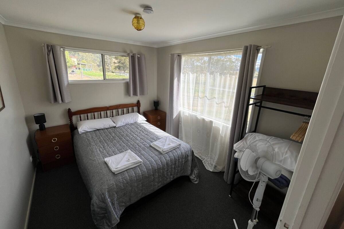 A bedroom with a bed, bedside tables, a window with curtains, a bunk bed, and a ceiling fan.