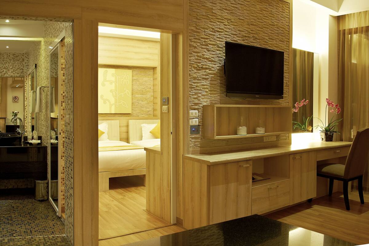 A modern hotel room with a wooden desk, a flat-screen TV, a bed, and a bathroom with a shower and sink.