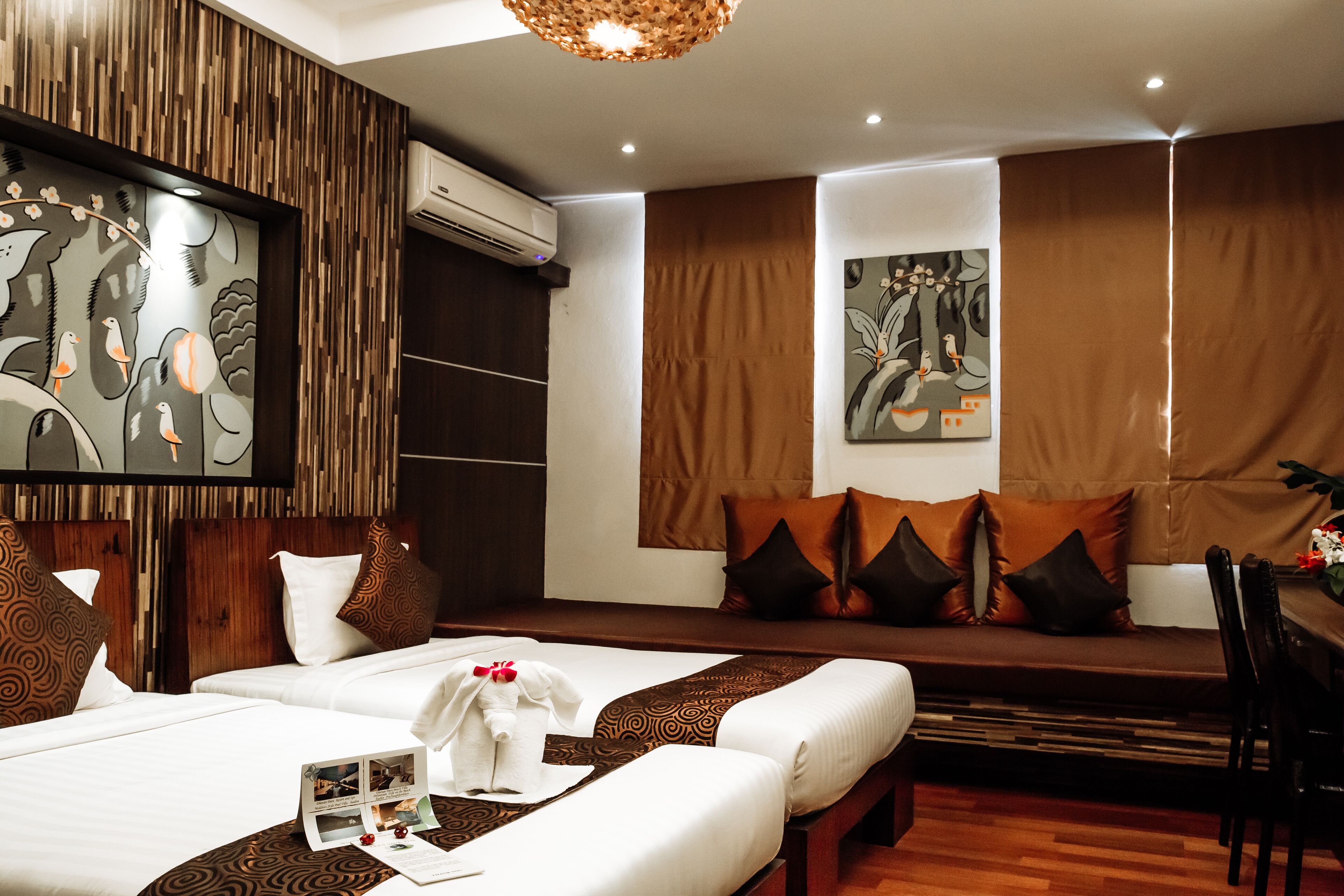 Habitación de hotel con dos camas, cabecero de madera, aire acondicionado de pared, un cuadro y una zona de comedor con mesa y sillas.