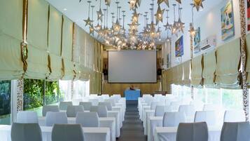 Un salón de conferencias con sillas blancas, una pantalla de proyector y lámparas colgantes con forma de estrella.