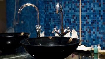 Un baño con un lavabo negro, un grifo cromado y una pared de azulejos de mosaico azul.