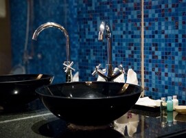 Un baño con un lavabo negro, un grifo cromado y una pared de azulejos de mosaico azul.