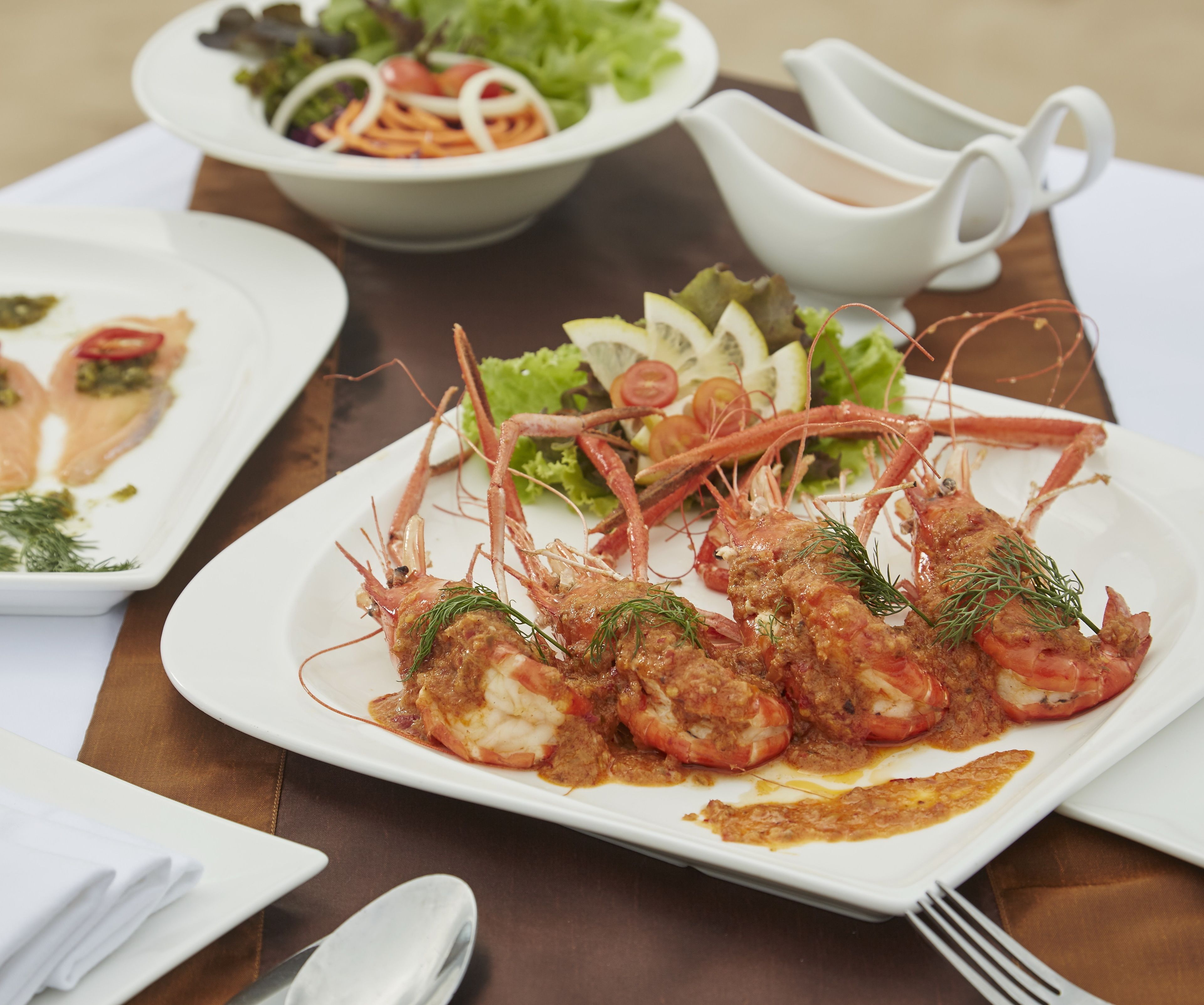 A dining table with plates of food, including shrimp and salad.