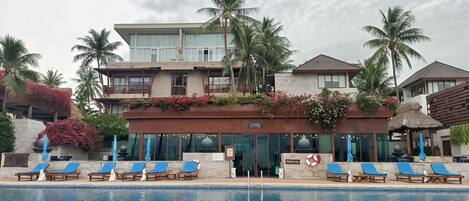 A resort with a swimming pool, lounge chairs, and palm trees.