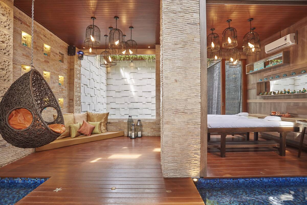 A spa room with a wooden floor, hanging light fixtures, a massage table, and a stone wall.