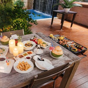 An outdoor dining area with a pool in the background, featuring a variety of dishes and drinks. - Dhevan Dara Beach Villa (Prachuap Khiri Khan)