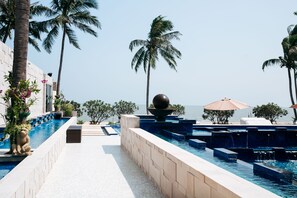 A pool area with clear blue water, palm trees, and a view of the sea. - Dhevan Dara Beach Villa (Prachuap Khiri Khan)