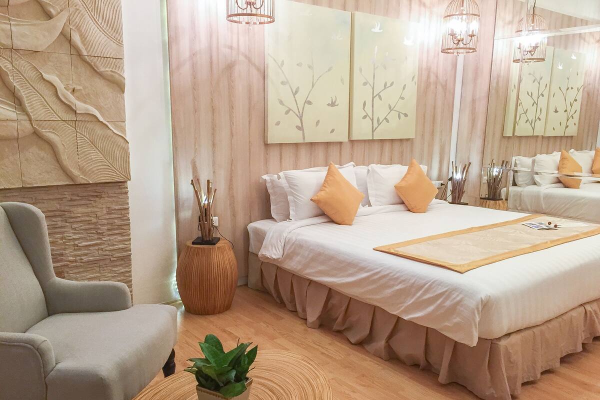 A modern hotel room with a large bed, a seating area with a chair, a small table with a plant, and wall art.
