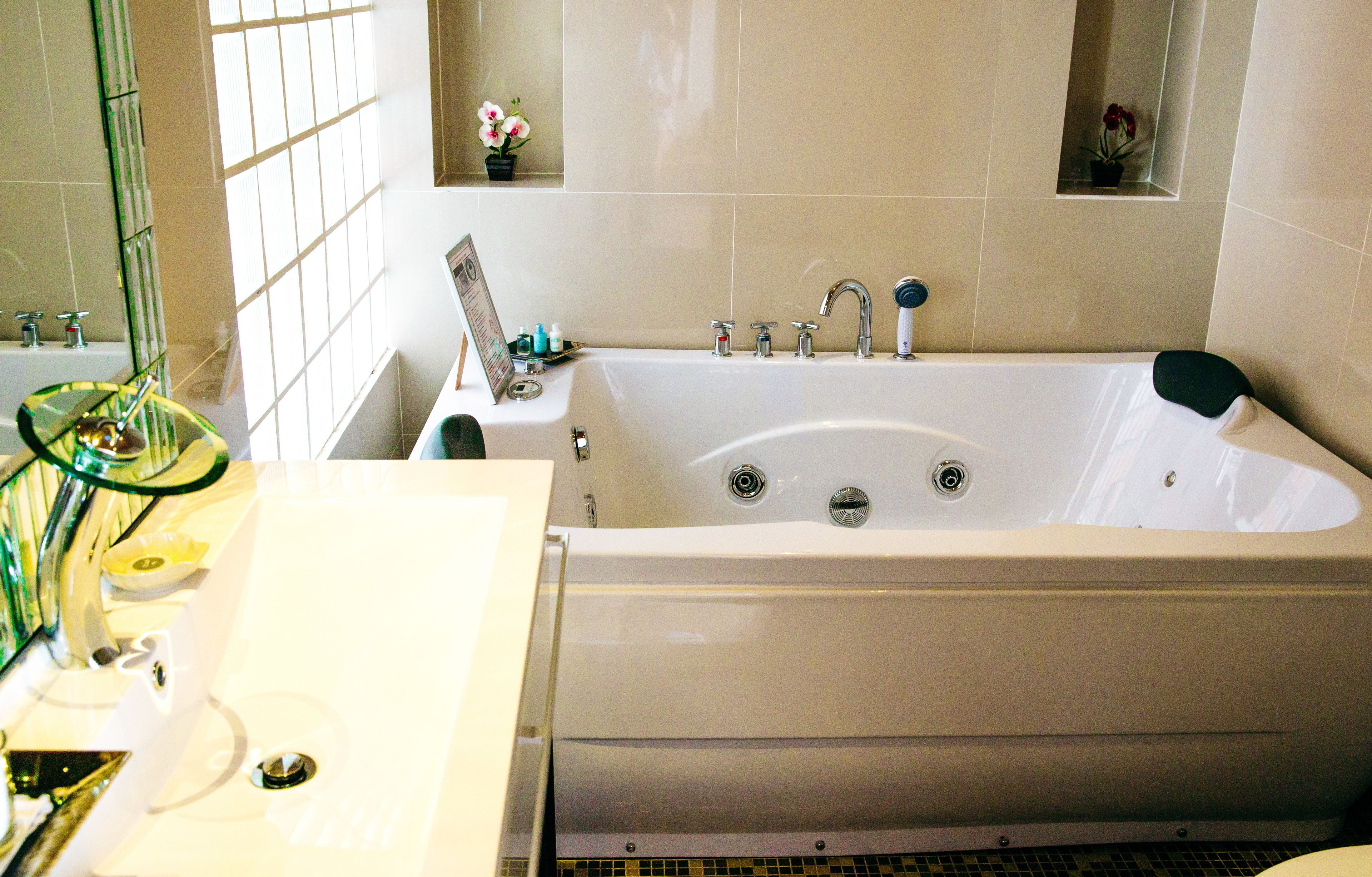 A bathroom with a large bathtub, a sink, and a mirror. There are two small flower arrangements on the wall.