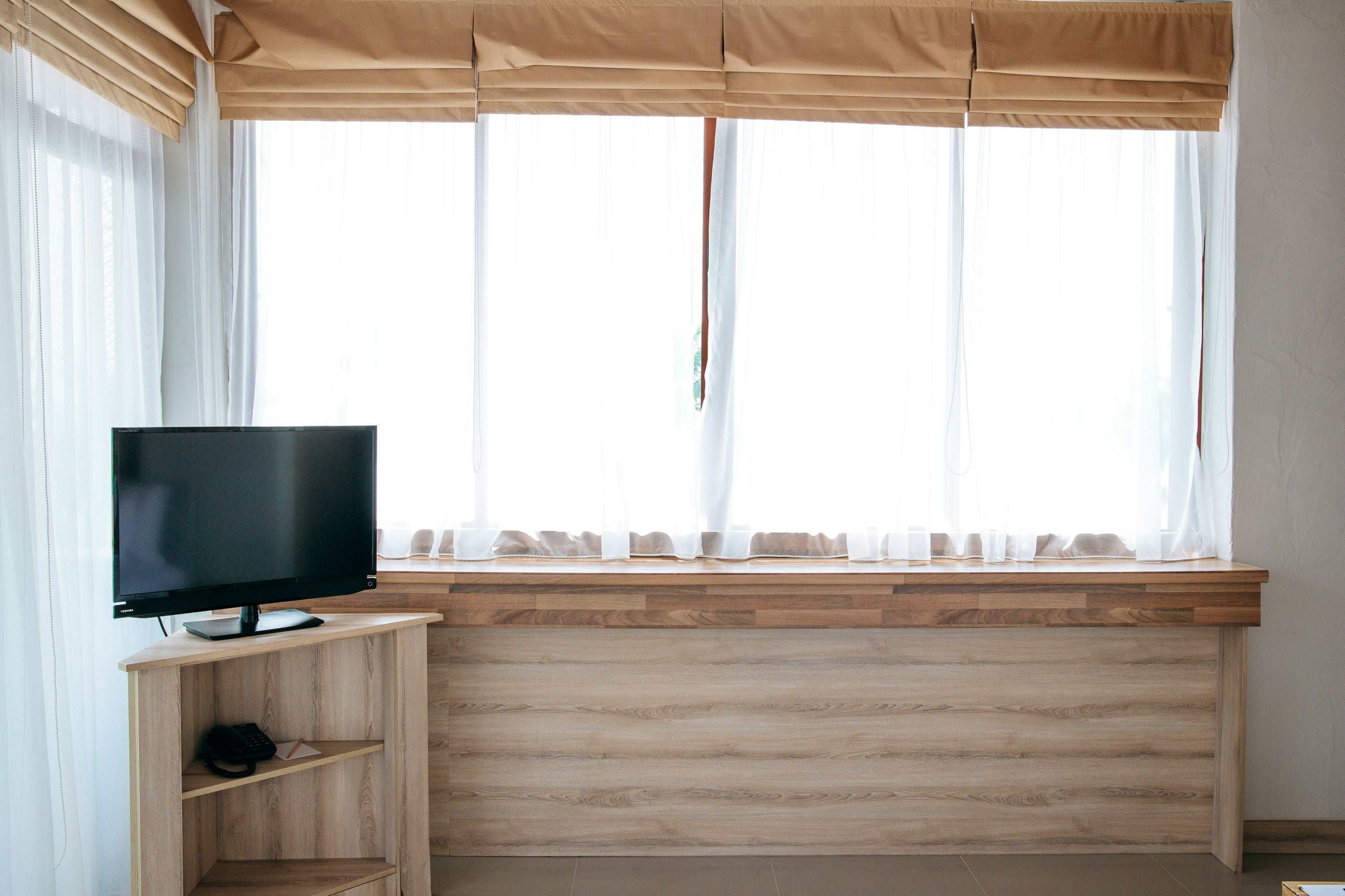 A room with a wooden desk, a television, and a window with sheer curtains.