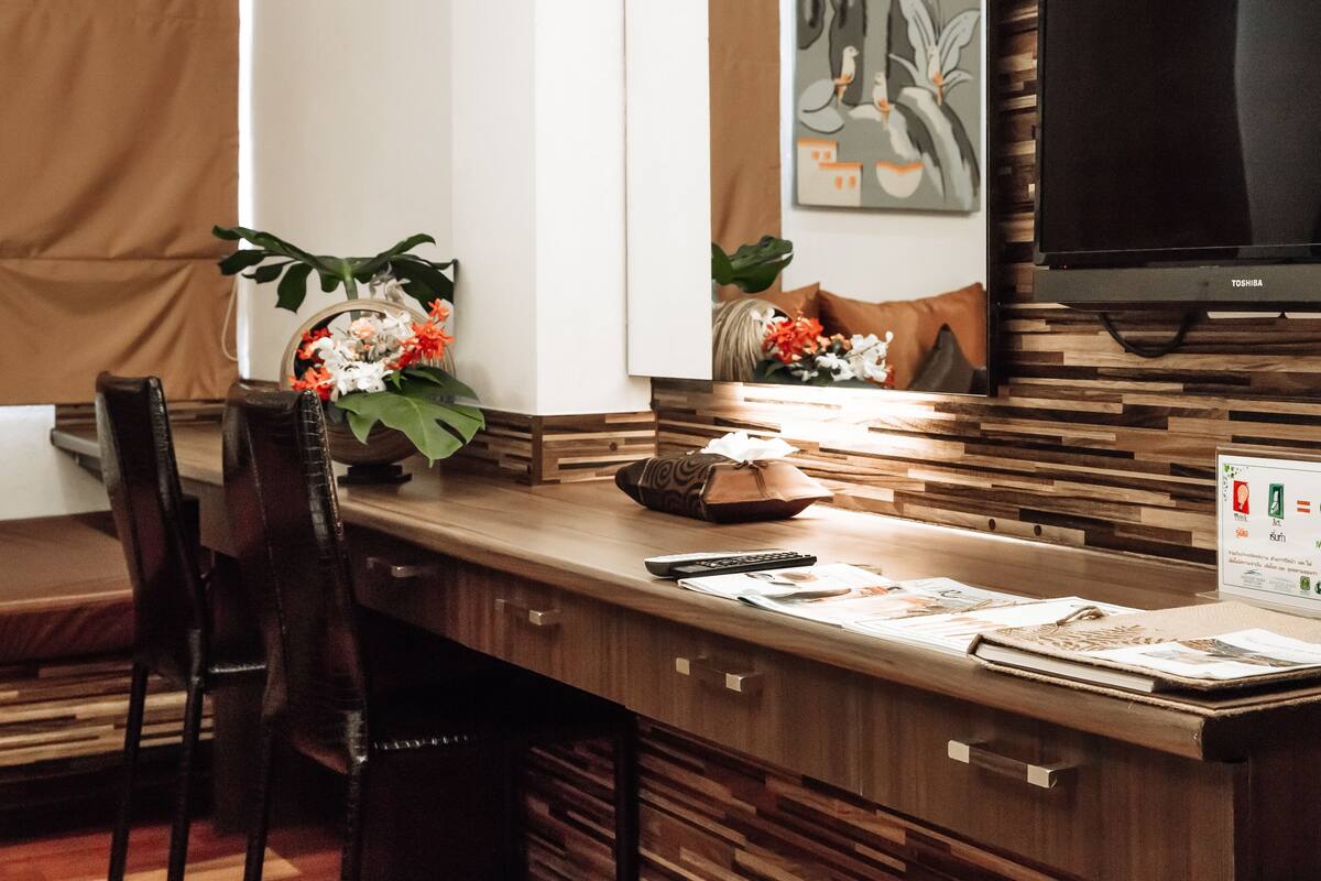 A wooden desk with a flat-screen TV, a chair, and a vase of flowers.