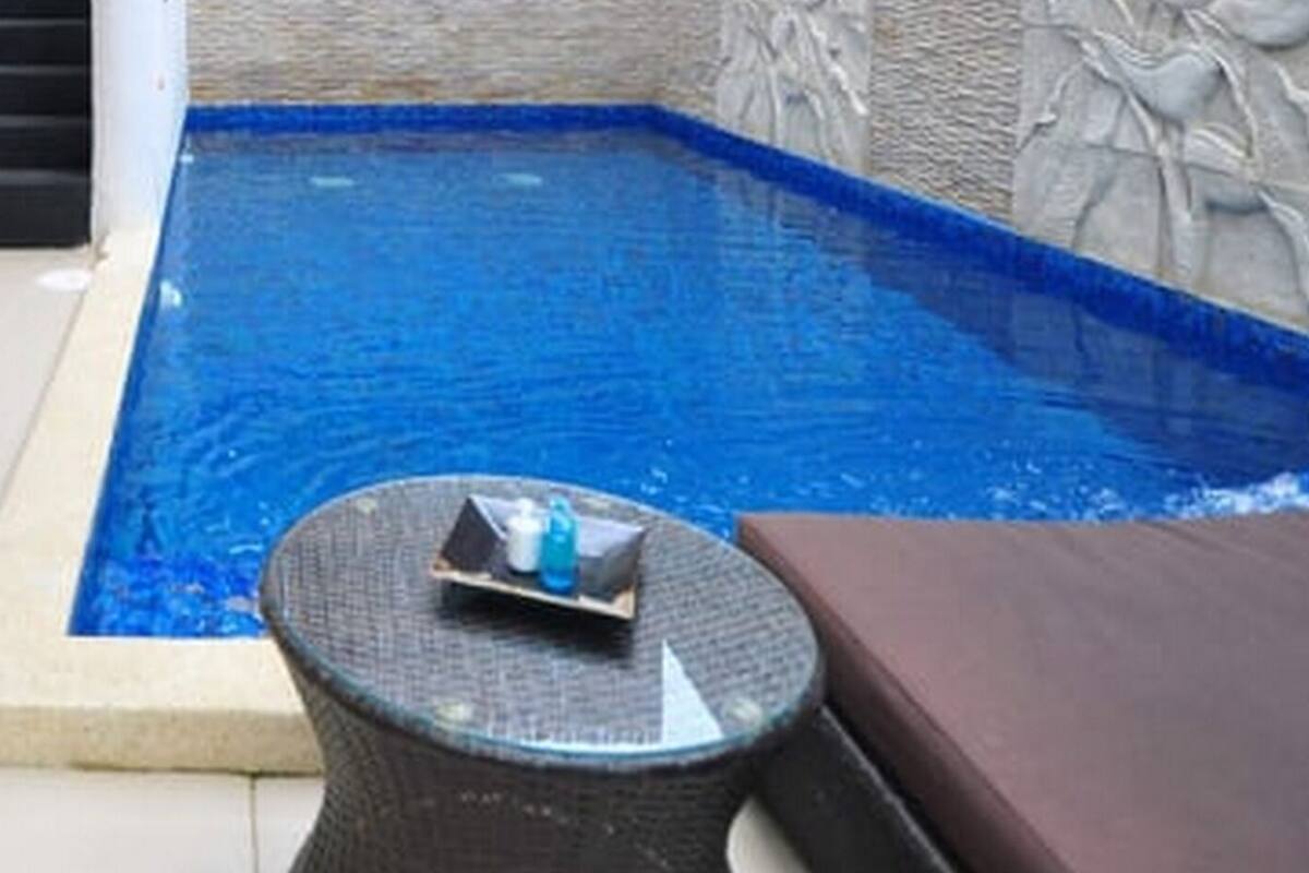 A small indoor pool with a tiled edge, a wicker chair, and a stone wall with carvings.