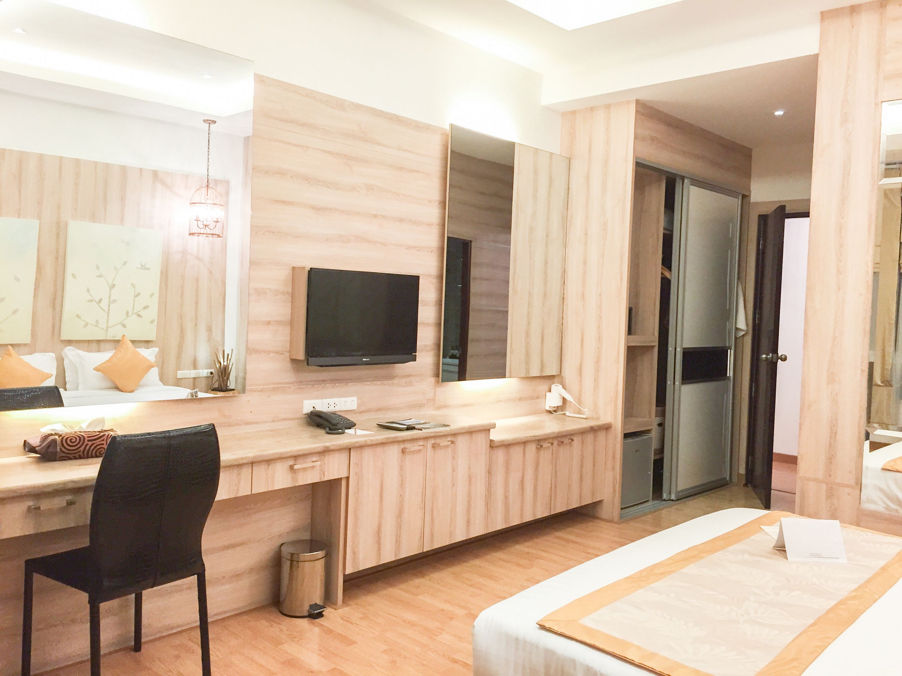 Une chambre d’hôtel moderne équipée d’une coiffeuse en bois, d’un téléviseur à écran plat, d’un bureau avec une chaise, d’un lit et d’une poubelle.