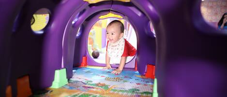 A child in a tunnel play area with colorful play mats and purple walls.