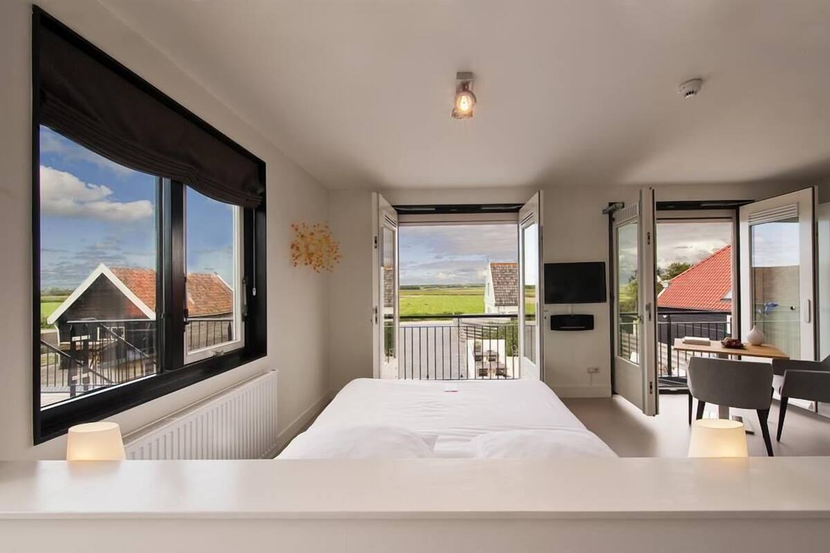 A bedroom with a large window, a bed, a desk, and a chair.