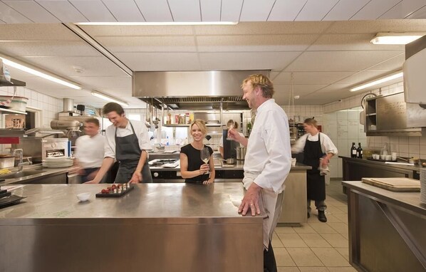 Cucina professionale con piani in acciaio inossidabile, isola centrale e diverse attrezzature da cucina.