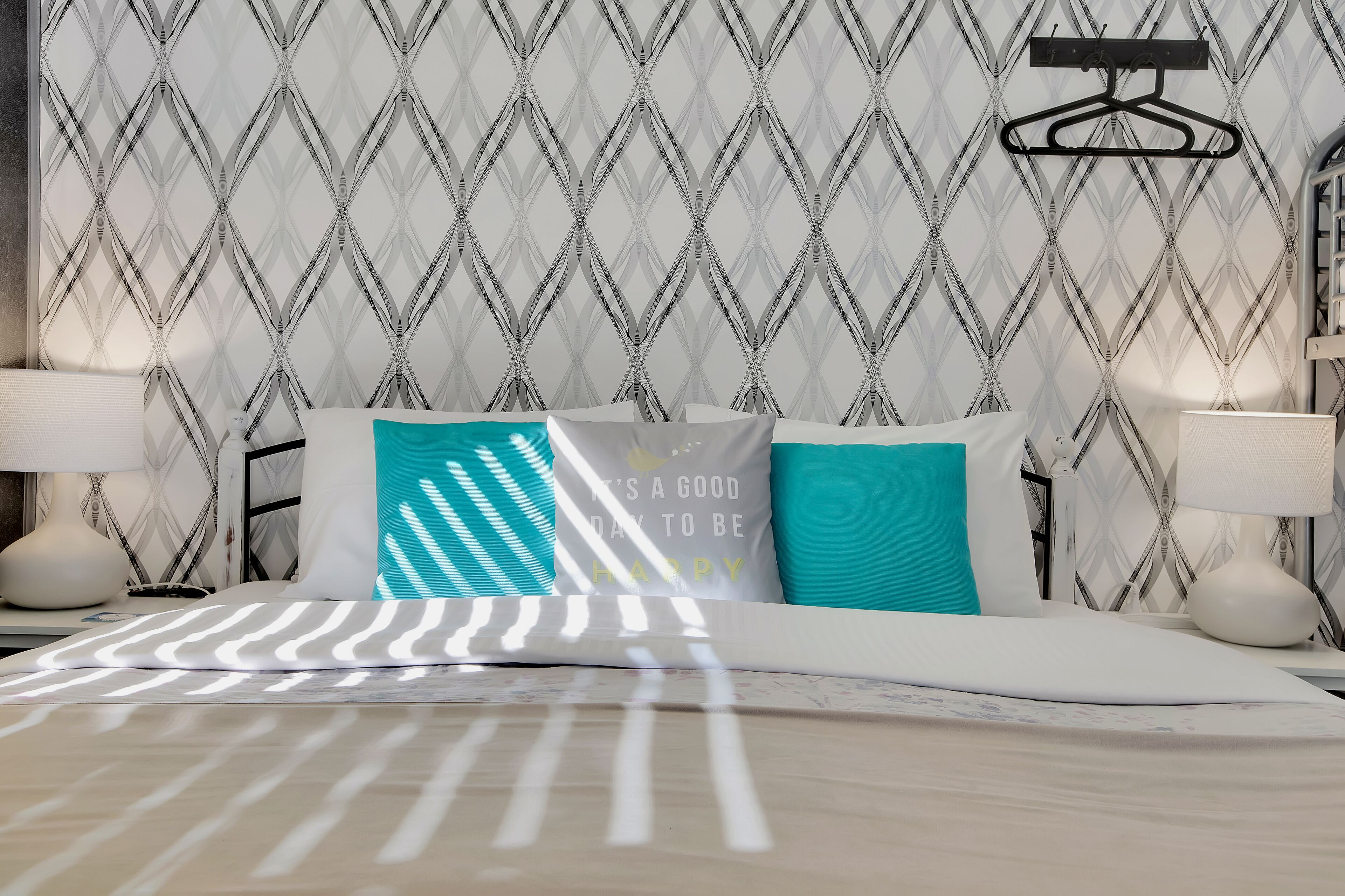 Una cama bien hecha con ropa de cama a rayas, un papel tapiz estampado y un perchero negro colgado.
