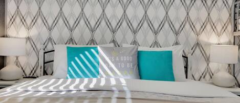 A neatly made bed with striped bedding, a patterned wall, and a hanging black hanger.