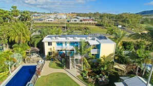 Un bâtiment à deux étages doté d’une piscine, entouré d’une végétation tropicale et surplombant un ciel dégagé.