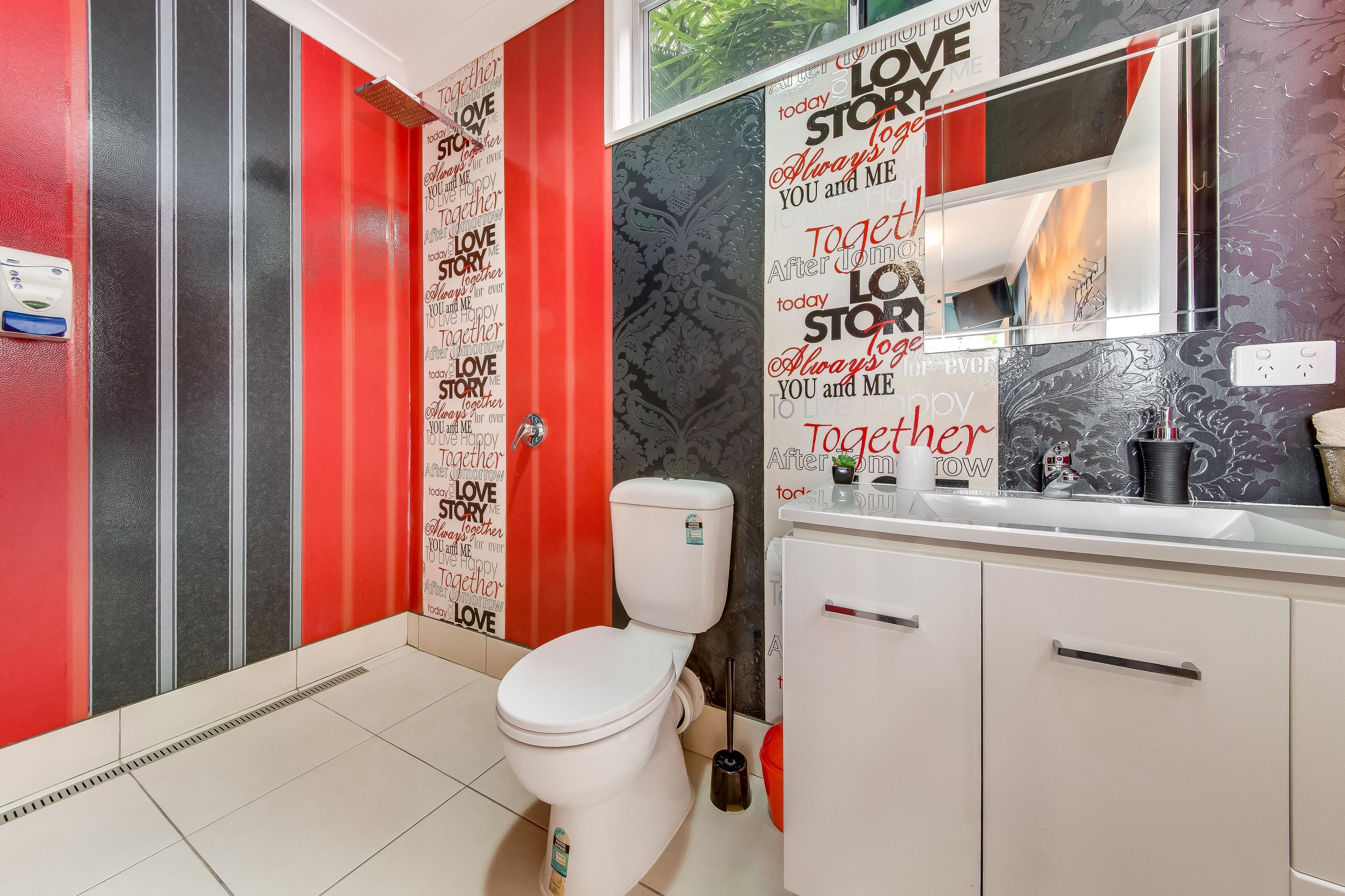 A bathroom with a white toilet, a red and black striped shower, and a vanity with a mirror.
