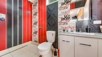 A bathroom with a white toilet, a red and black striped shower, and a vanity with a mirror.