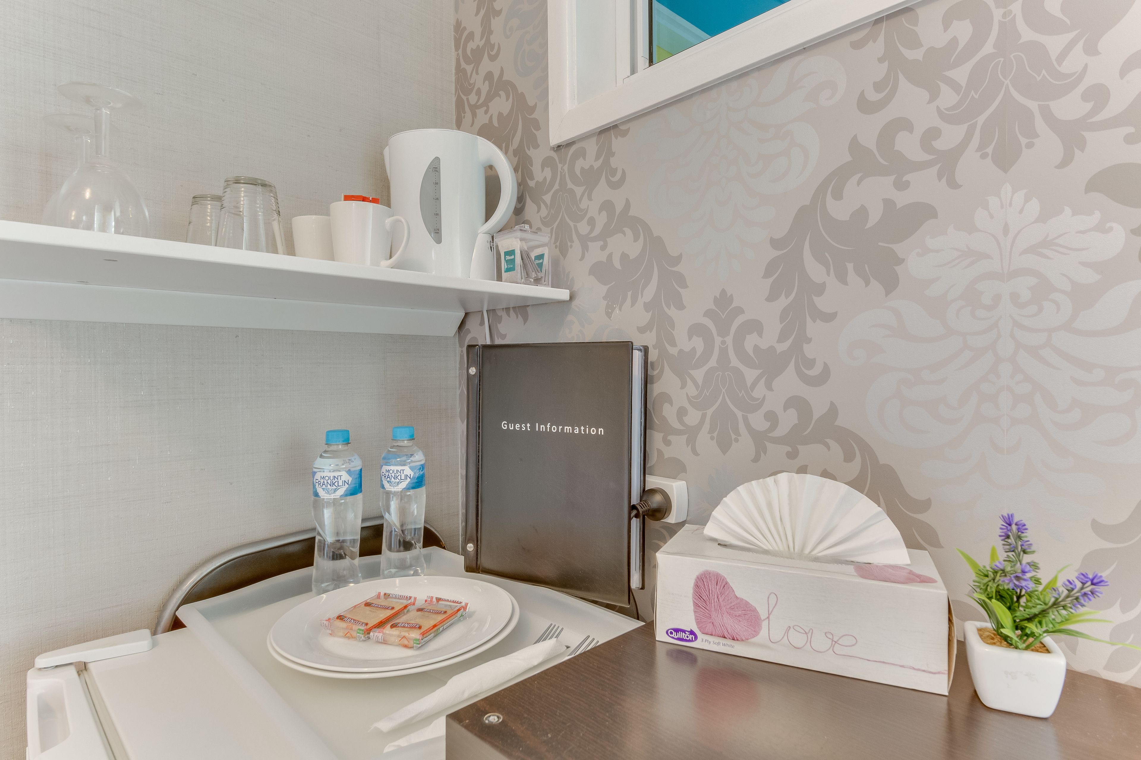 A hotel room with a dining area featuring a table set for two, a water dispenser, a coffee maker, and a guest information board.