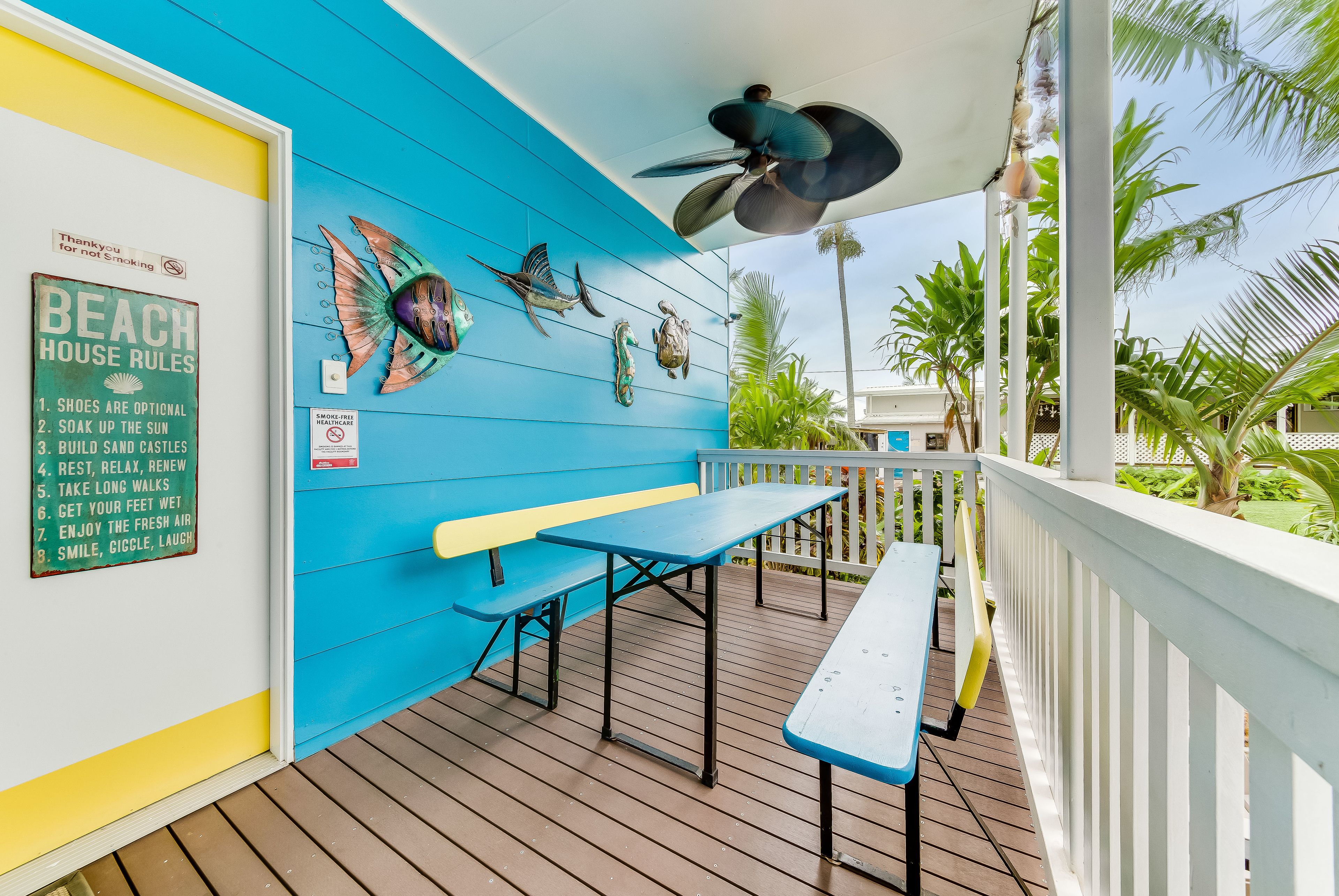 A covered outdoor area with a blue wall, a ceiling fan, and a sign listing beach house rules.