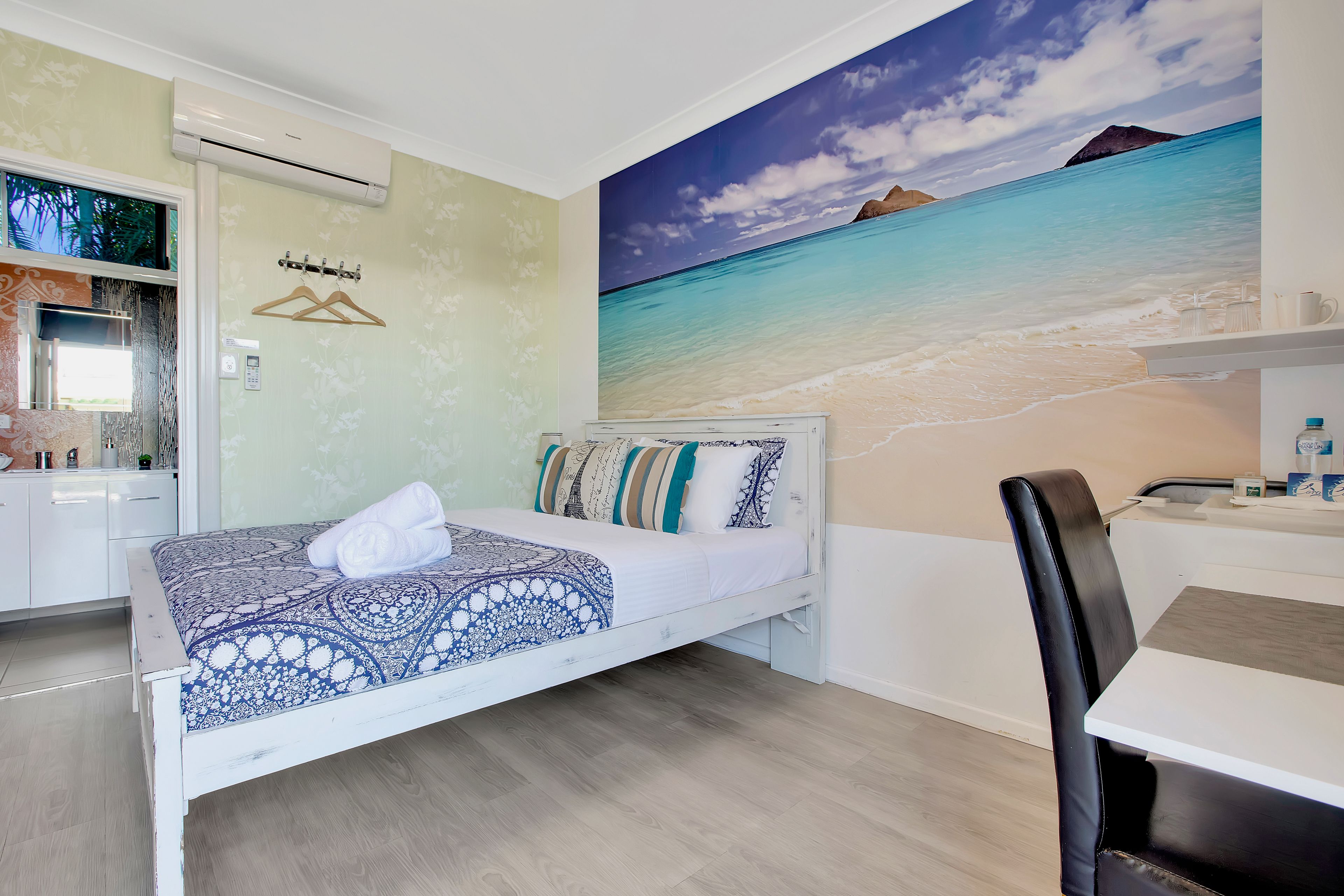Une chambre à coucher avec un lit, un bureau et une chaise. Il y a un tableau représentant une plage accroché au mur.