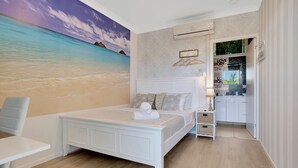 Une chambre avec un grand décor mural représentant une plage, un lit blanc, une petite table de chevet et une armoire.