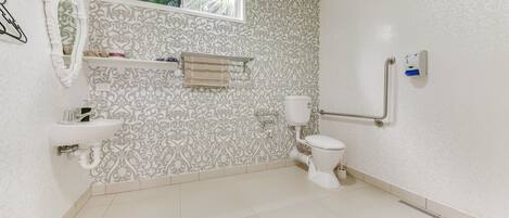 Une salle de bain avec un mur à motifs, une fenêtre, un lavabo, des toilettes et une barre d’appui.