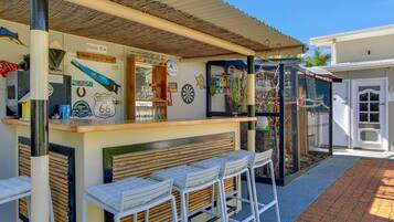 A beach bar with a rustic design, featuring a counter with stools, a dartboard, and various decorations.