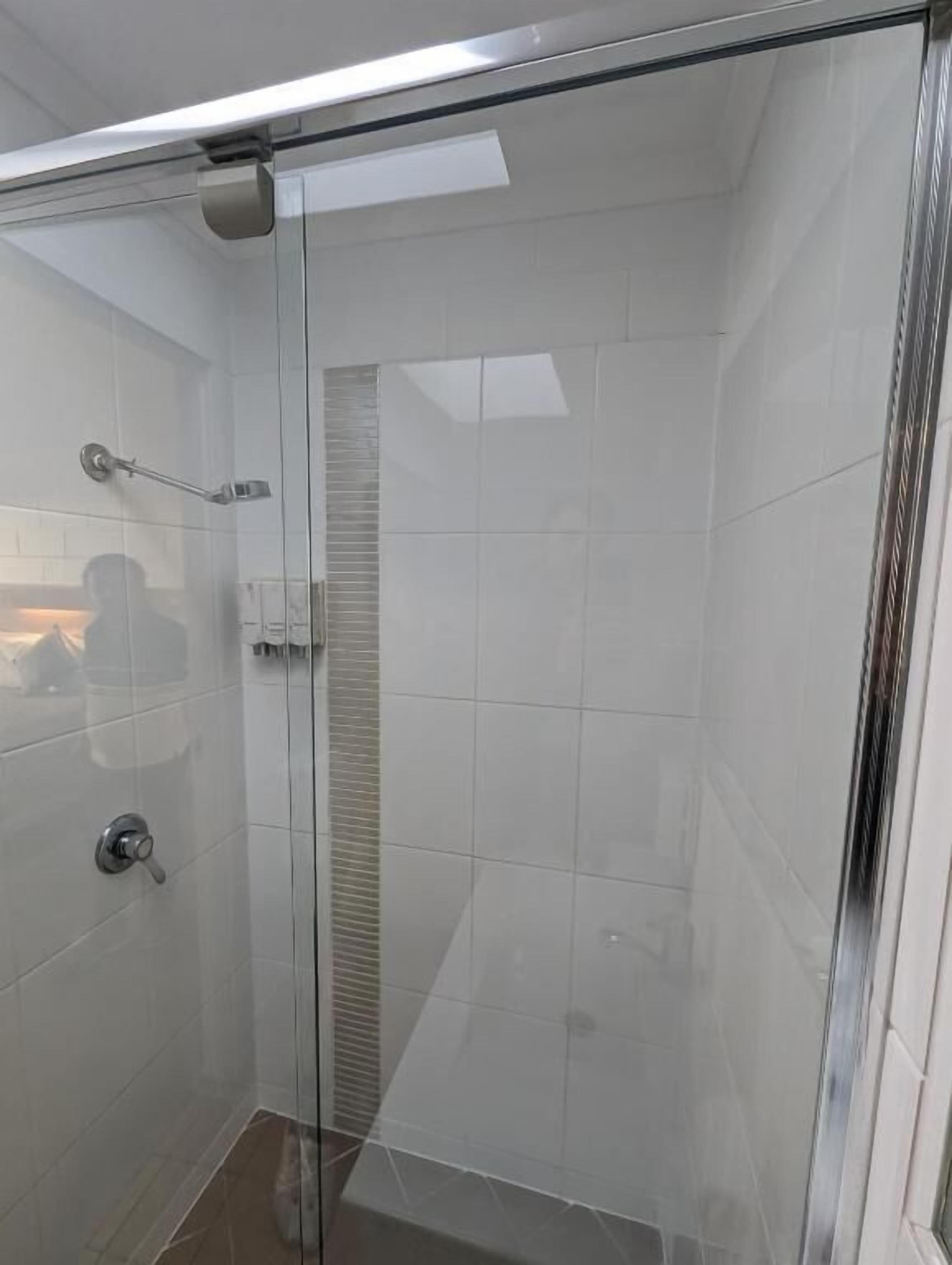 Ducha con cerramiento de vidrio, azulejos blancos y panel de control visible.