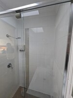 Ducha con cerramiento de vidrio, azulejos blancos y panel de control visible.