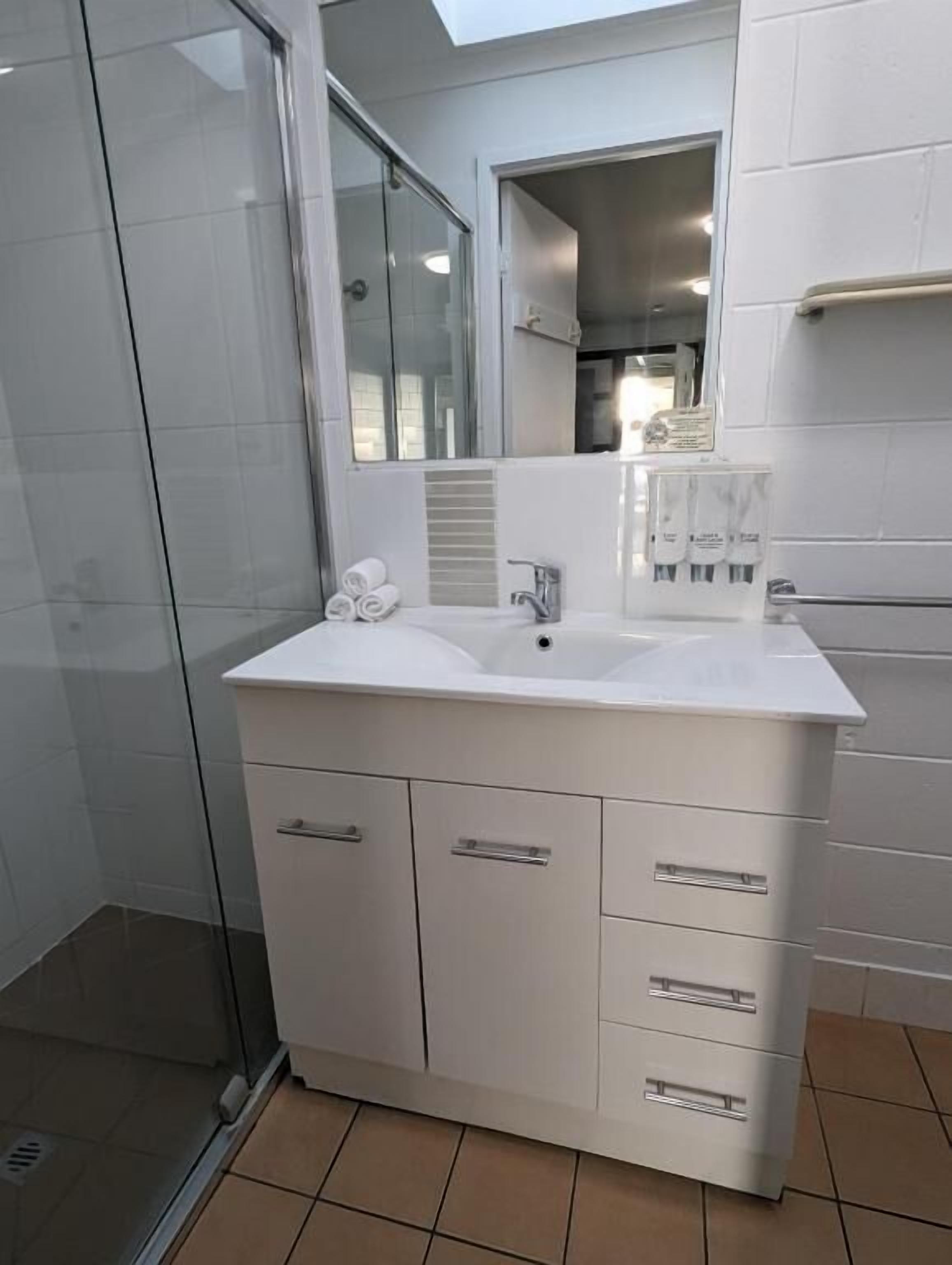 A modern bathroom with a glass shower enclosure, a white vanity with a sink, and a mirror above it.