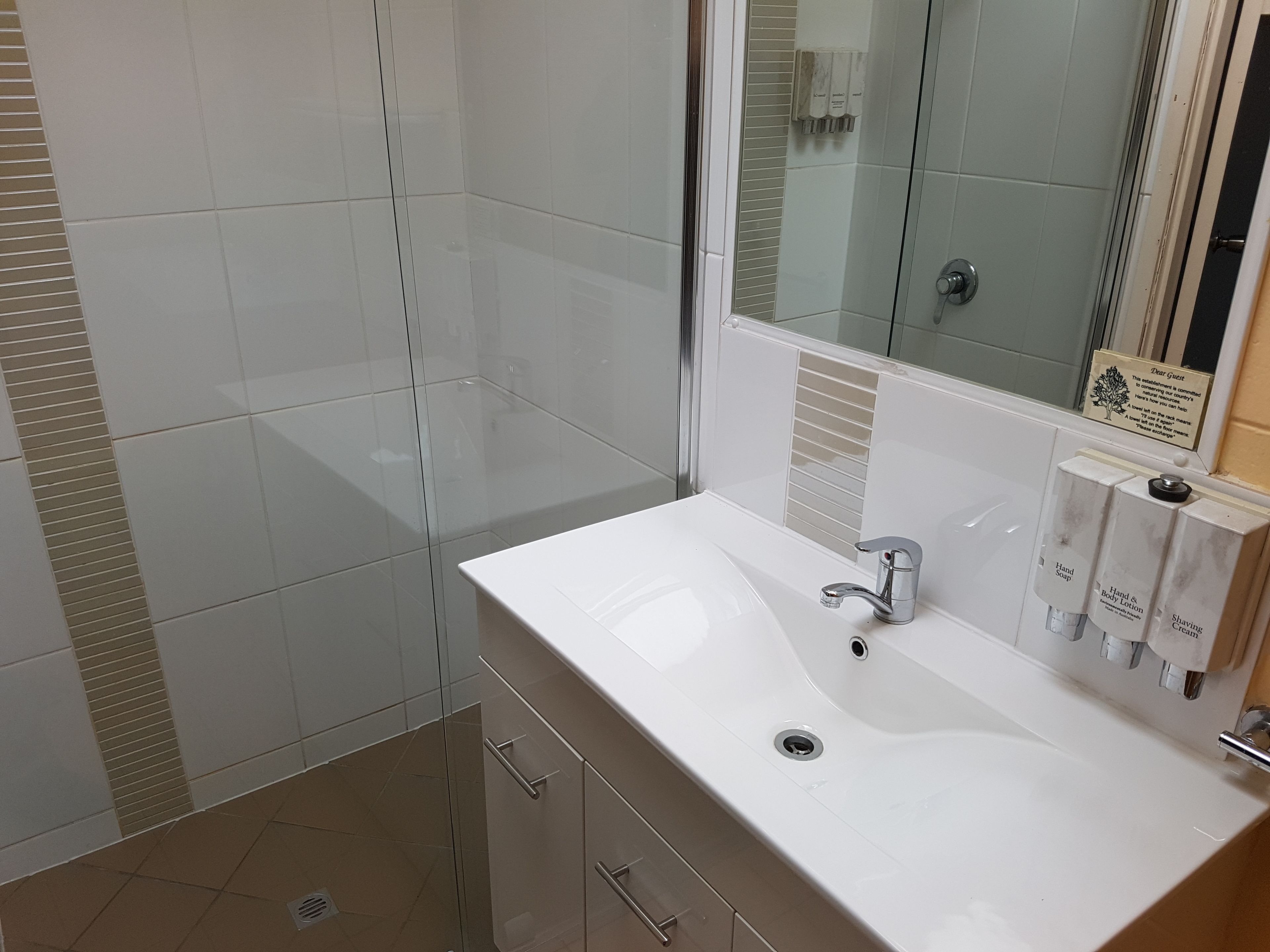 A modern bathroom with a large mirror, a white sink, and a shower area.