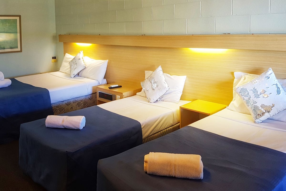 Ett hotellrum med tre separata sängar, var och en med en kudde och en hoprullad handduk.