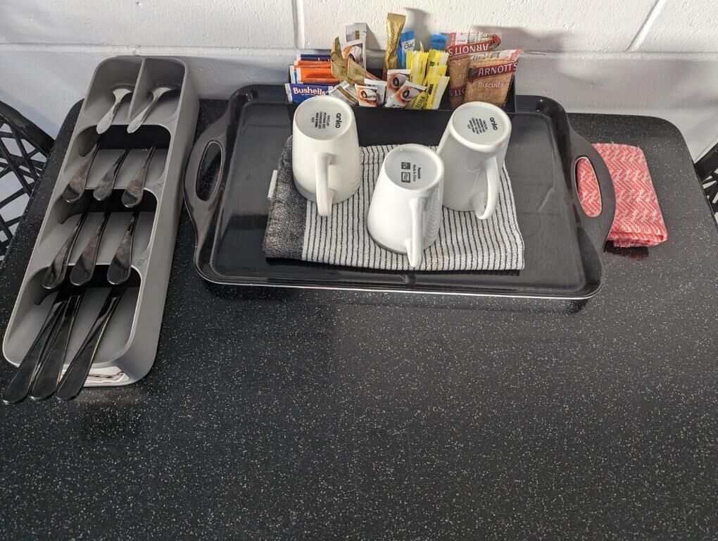 A kitchen counter with a tray holding three white mugs, a knife block, and a red napkin.