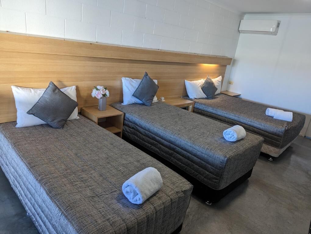 A hotel room with three single beds, each with a pillow and a rolled towel.