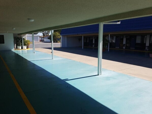 A covered outdoor area with a blue floor, white pillars, and a building with a blue roof in the background.