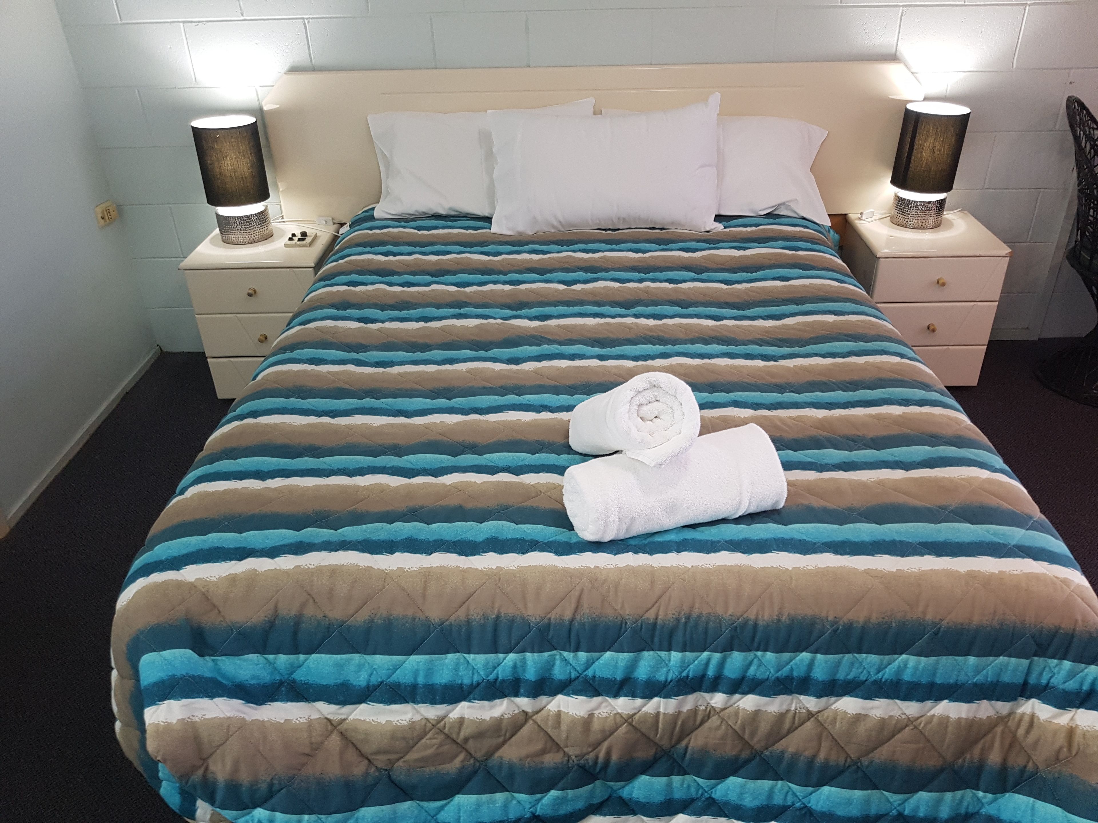 Una cama bien hecha con ropa de cama a rayas, dos lámparas de noche y una toalla doblada sobre la cama.