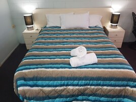 Una cama bien hecha con ropa de cama a rayas, dos lámparas de noche y una toalla doblada sobre la cama.