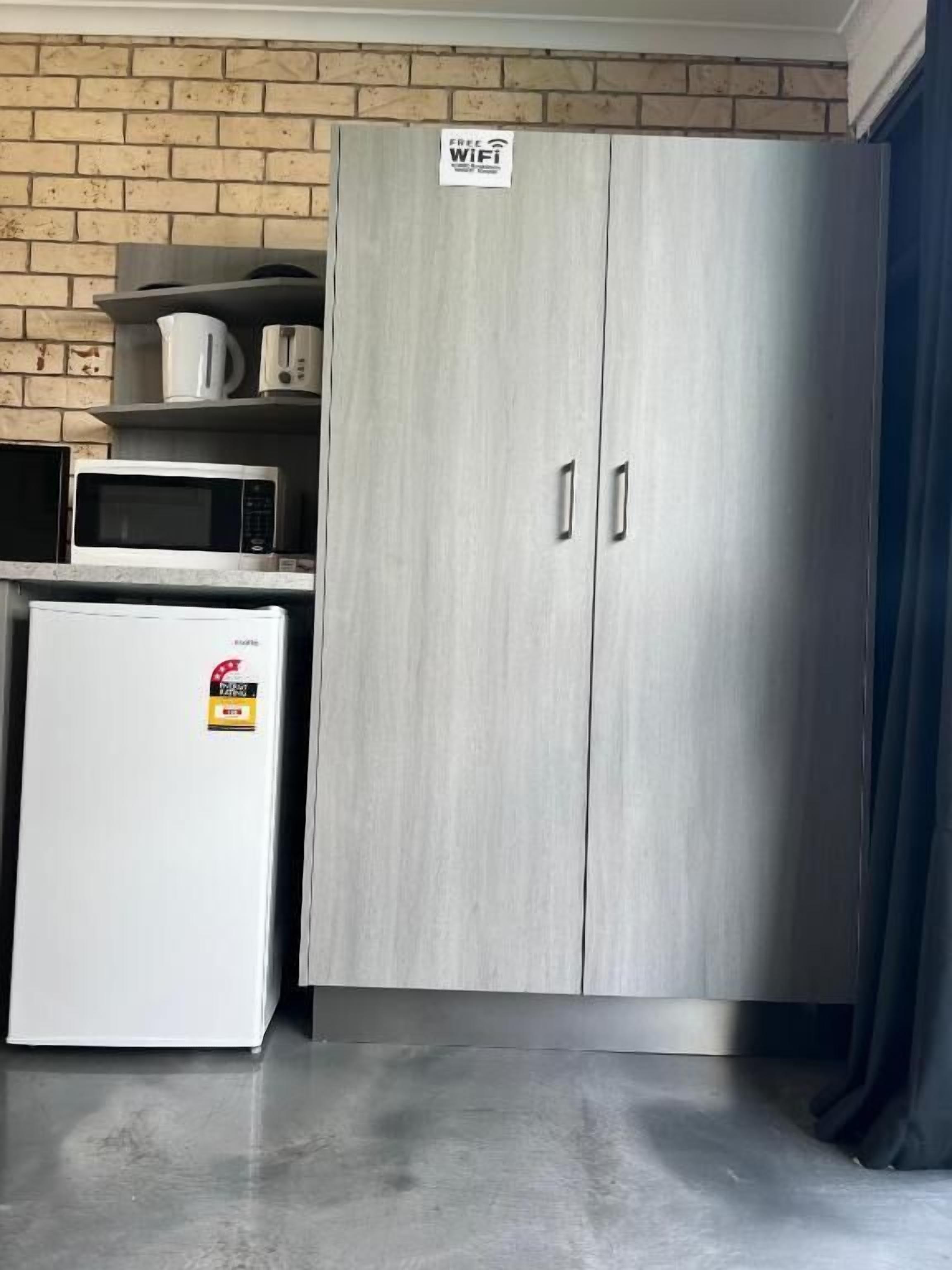 Uma cozinha compacta com micro-ondas, um frigorífico pequeno e um armário com a inscrição 'Wi-Fi Gratuito'.