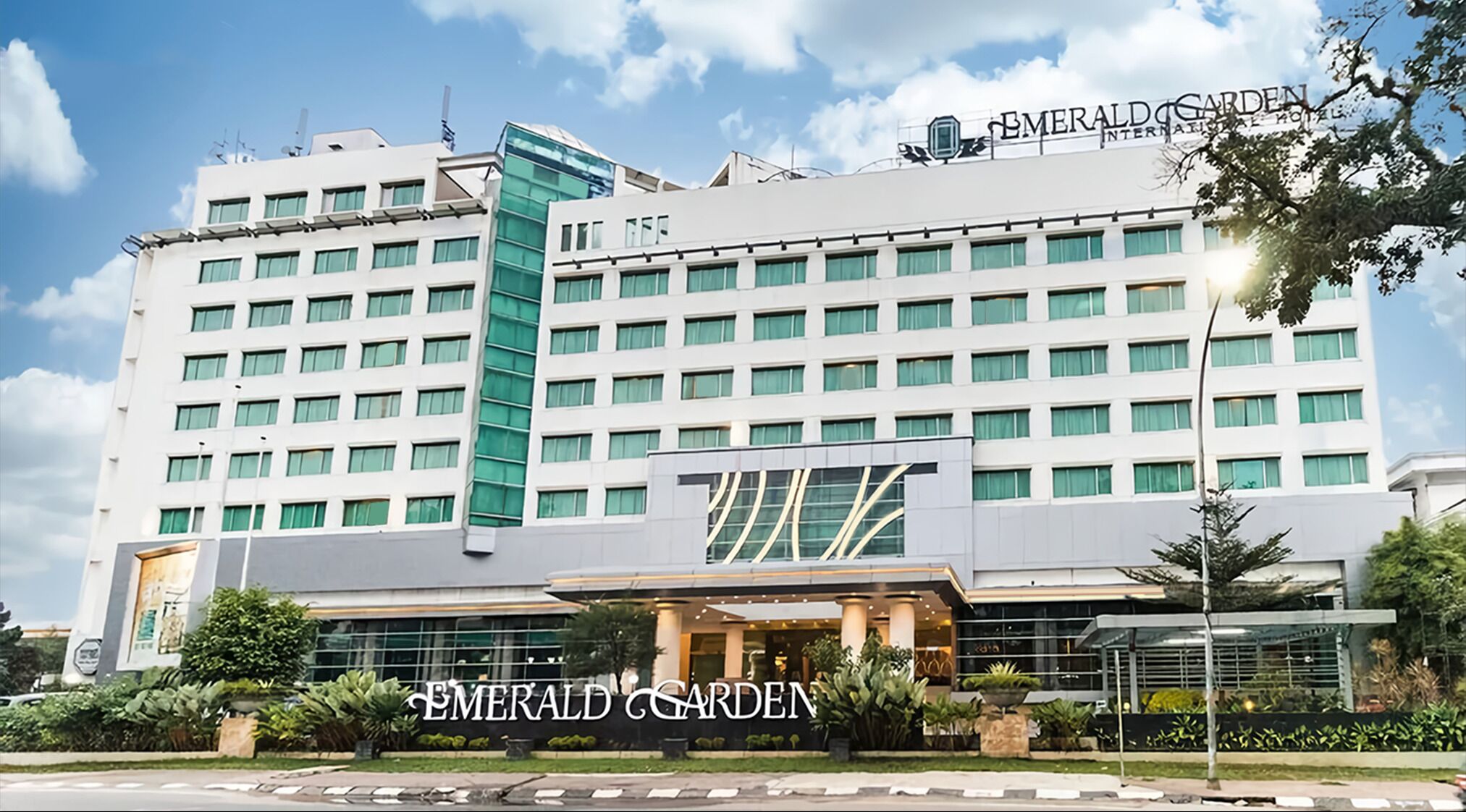 Un hôtel à plusieurs étages, reconnaissable à son enseigne bien visible indiquant : « Emerald Garden International Hotel ».