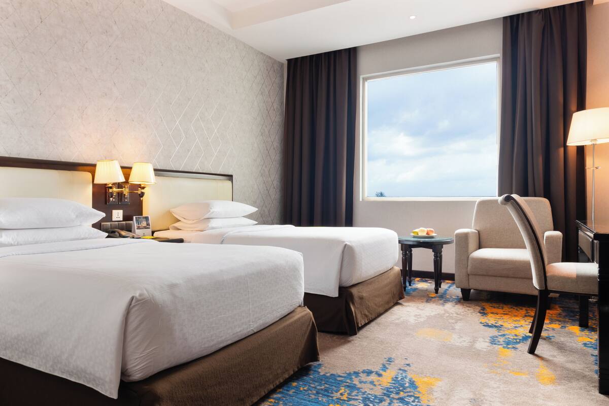 Una habitación de hotel con dos camas, un escritorio, una silla, una ventana con cortinas y una lámpara.