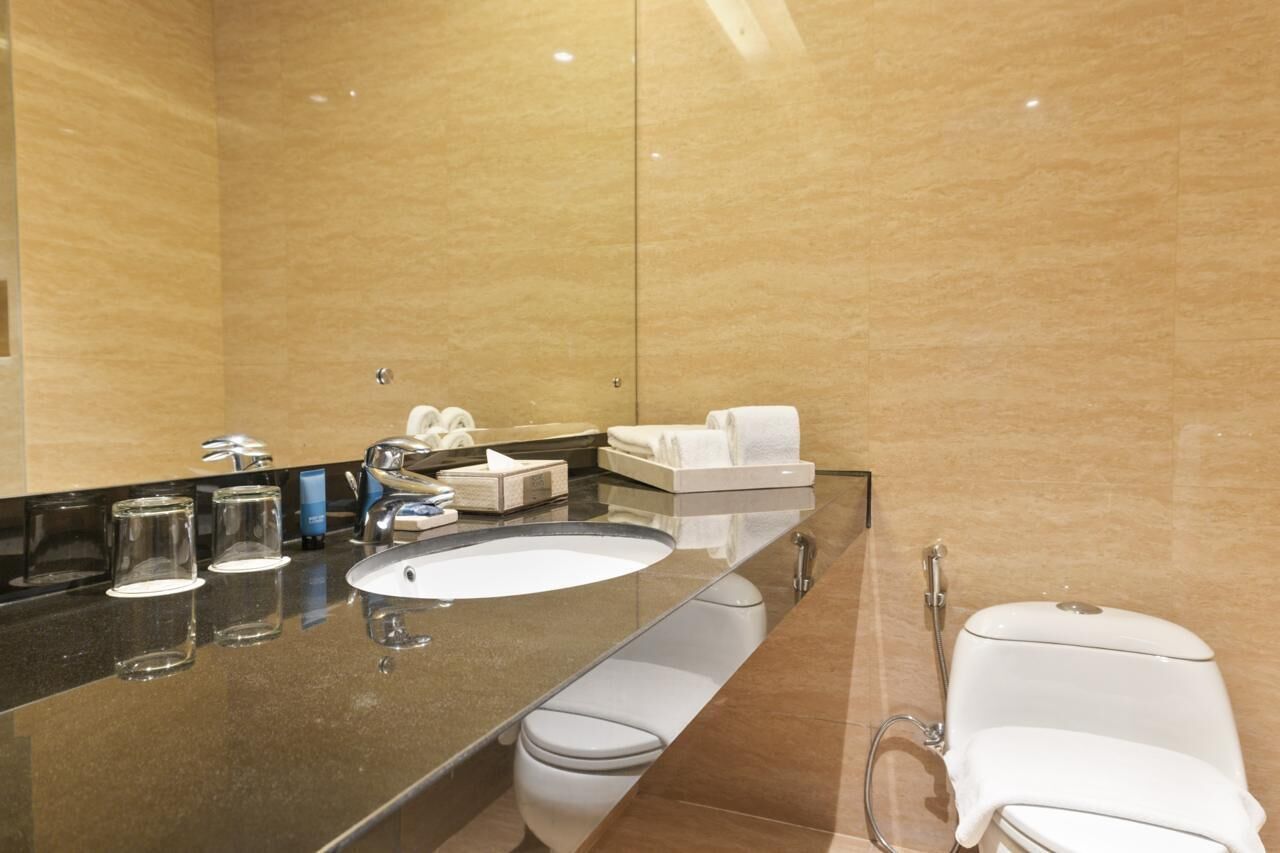 A modern bathroom with a large mirror, a round sink, a toilet, and a shower area.
