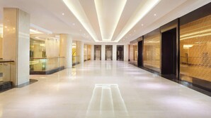 Un pasillo moderno de hotel con suelo reflectante, iluminación empotrada y puertas de vidrio que dan a las habitaciones.